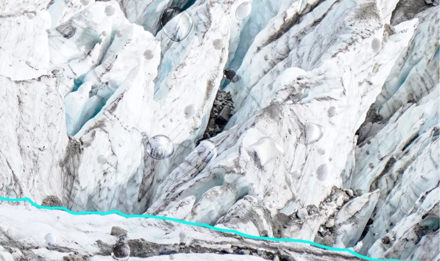 Crevasses d’un glacier blanc bleuté strié de gris, vue aérienne, avec une ligne turquoise au bas.