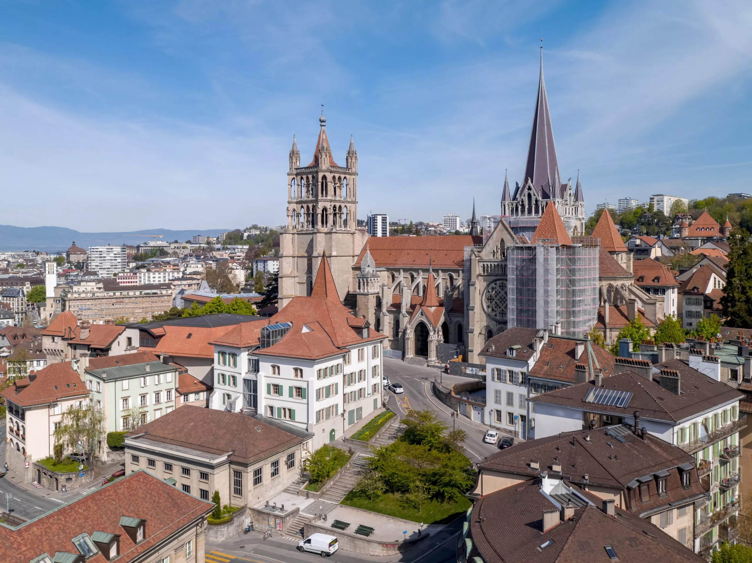 Vue de Lausanne et de la maison gaudard: cathédrale gothique à haute flèche, toits rouges, échafaudage, ciel bleu.